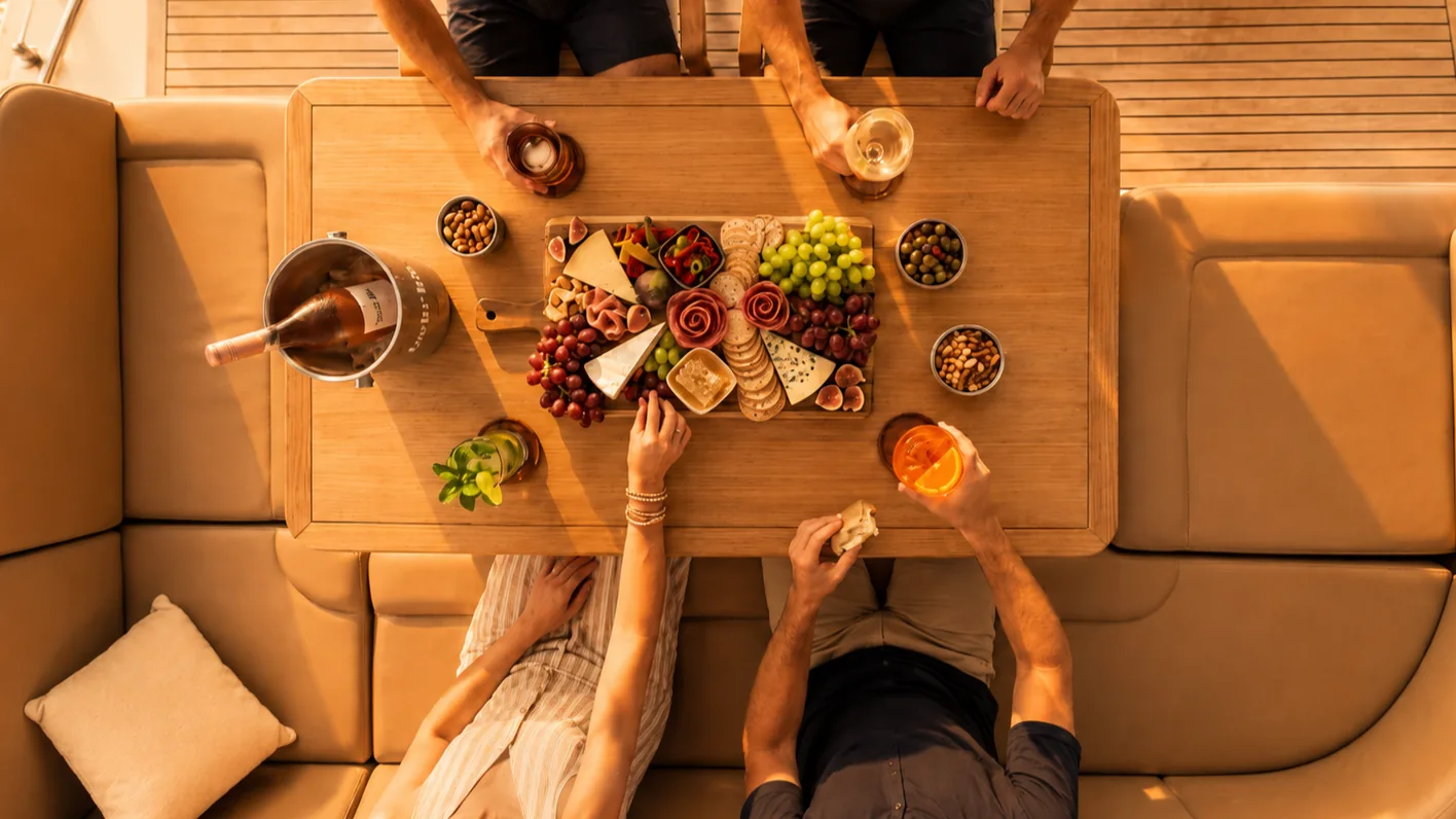 Overhead view of a charcuterie board and drinks on the deck of a private yacht charter in Destin, with guests gathered around the table