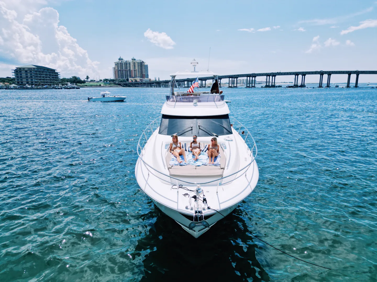 Yacht Charter on Destin Harbour Over Labor Day Weekend The Lovin’ Life yacht at anchor on clear turquoise water near the Destin bridge, guests seated on the bow with the harbour skyline behind