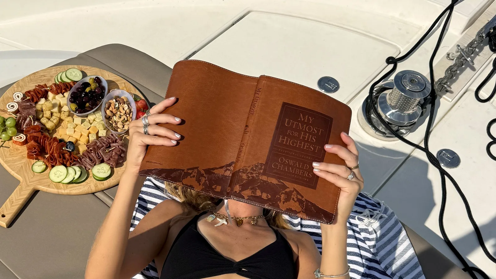 A Slow October Afternoon on a Destin Yacht Charter A guest reading on the sunpad of a private yacht charter in Destin beside a charcuterie board, with the bow deck and anchor line in view