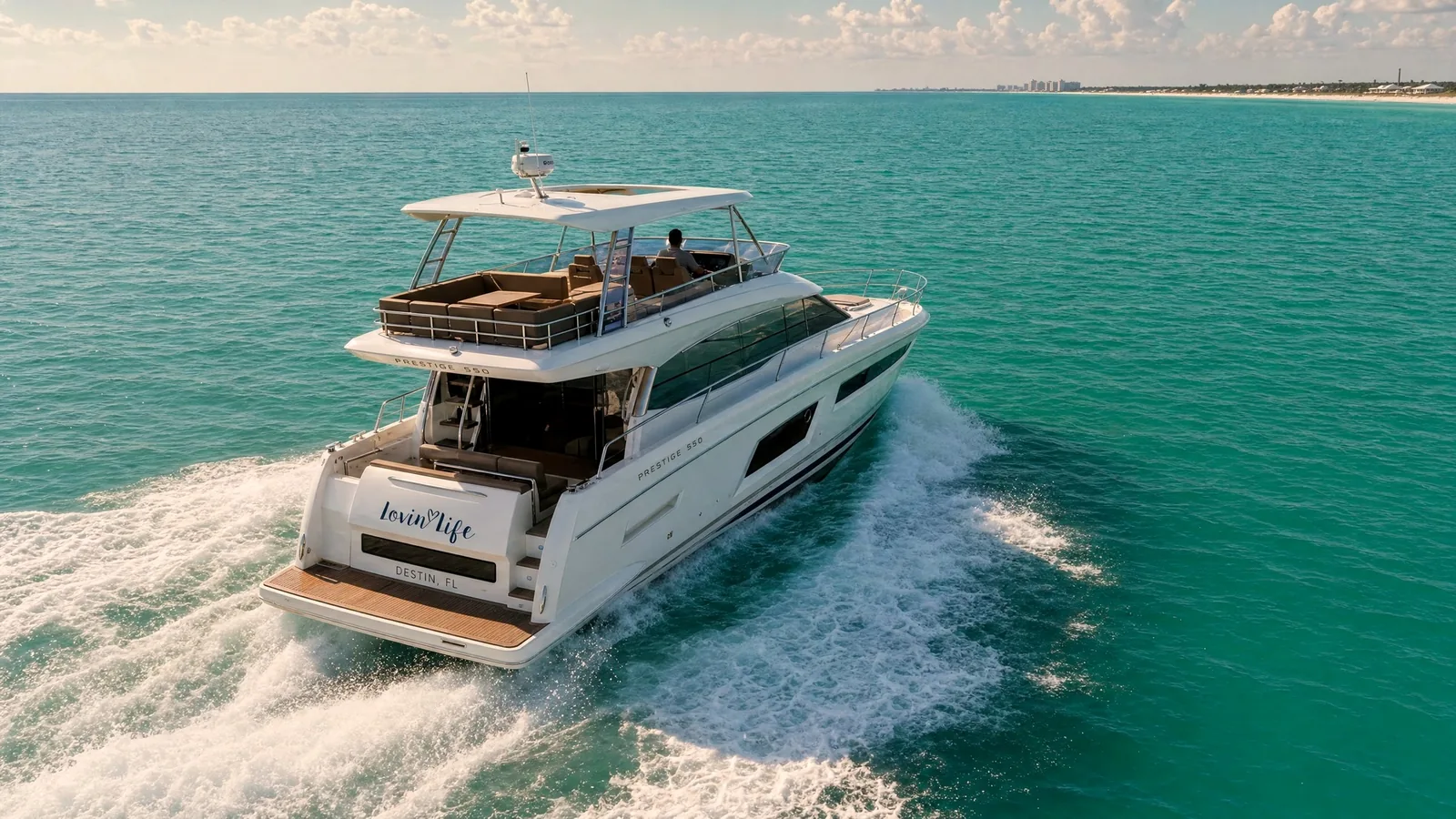 Lovin’ Life Cruising Open Emerald Water off Destin Aerial view of the Lovin’ Life, a Prestige 550 Flybridge, cruising across open emerald water off Destin with the shoreline in the distance