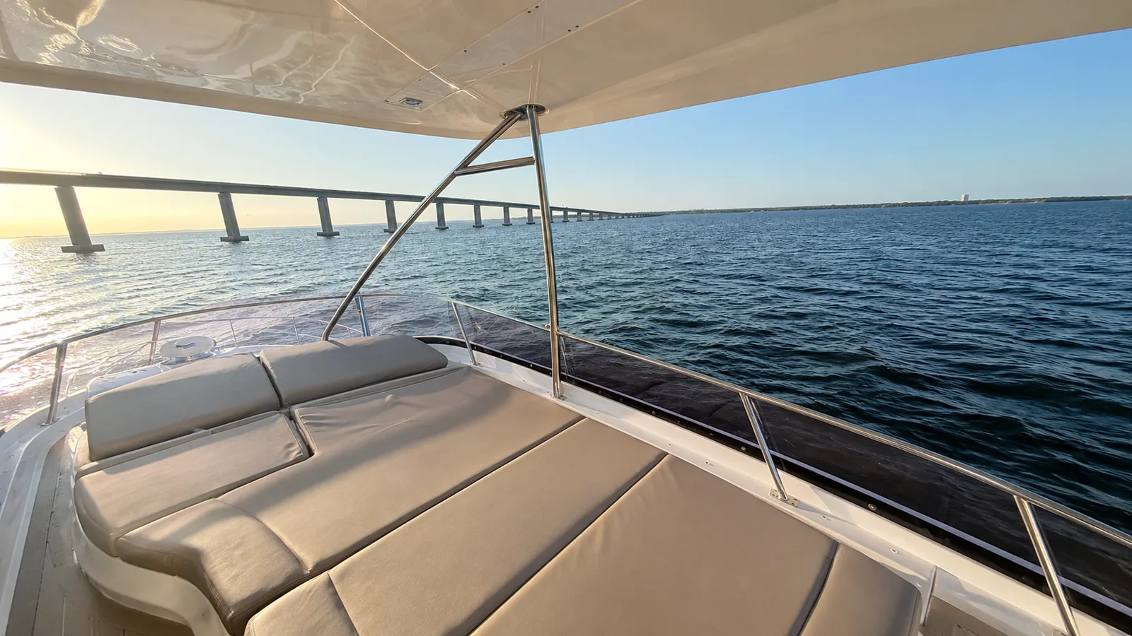 The forward sunpad of the Lovin’ Life at golden hour, looking past the bow rail toward the Destin bridge and calm open water